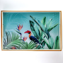 Load image into Gallery viewer, A rectangular gold-framed wall art print featuring a tropical design with large green palm and banana leaves, toucan birds, and pink bird-of-paradise flowers on a light aqua background.